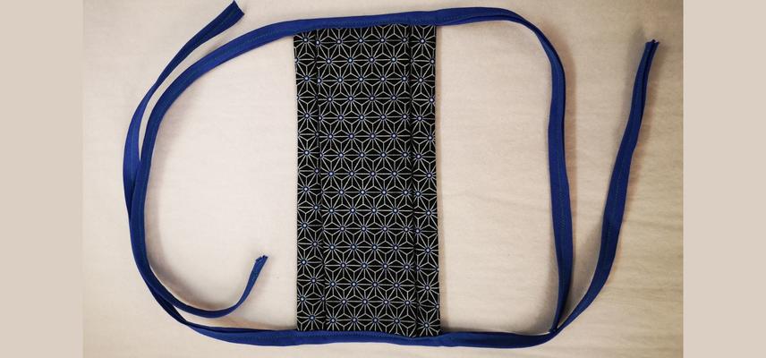 18497 Handmade face covering of black patterned cotton with blue tie straps