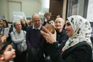 Muslim woman wearing patterned hijab (Islamic headscarf) giving a tour of the Museum, she is holding up a paper astrolabe to the audience. 