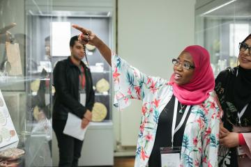 Muslim woman wearing pink hijab (Islamic headscarf) giving a tour of the Museum, she is pointing to an astrolabe in a case.